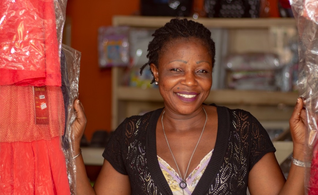 A smiling ASHA client standing in the doorway of her clothing shop